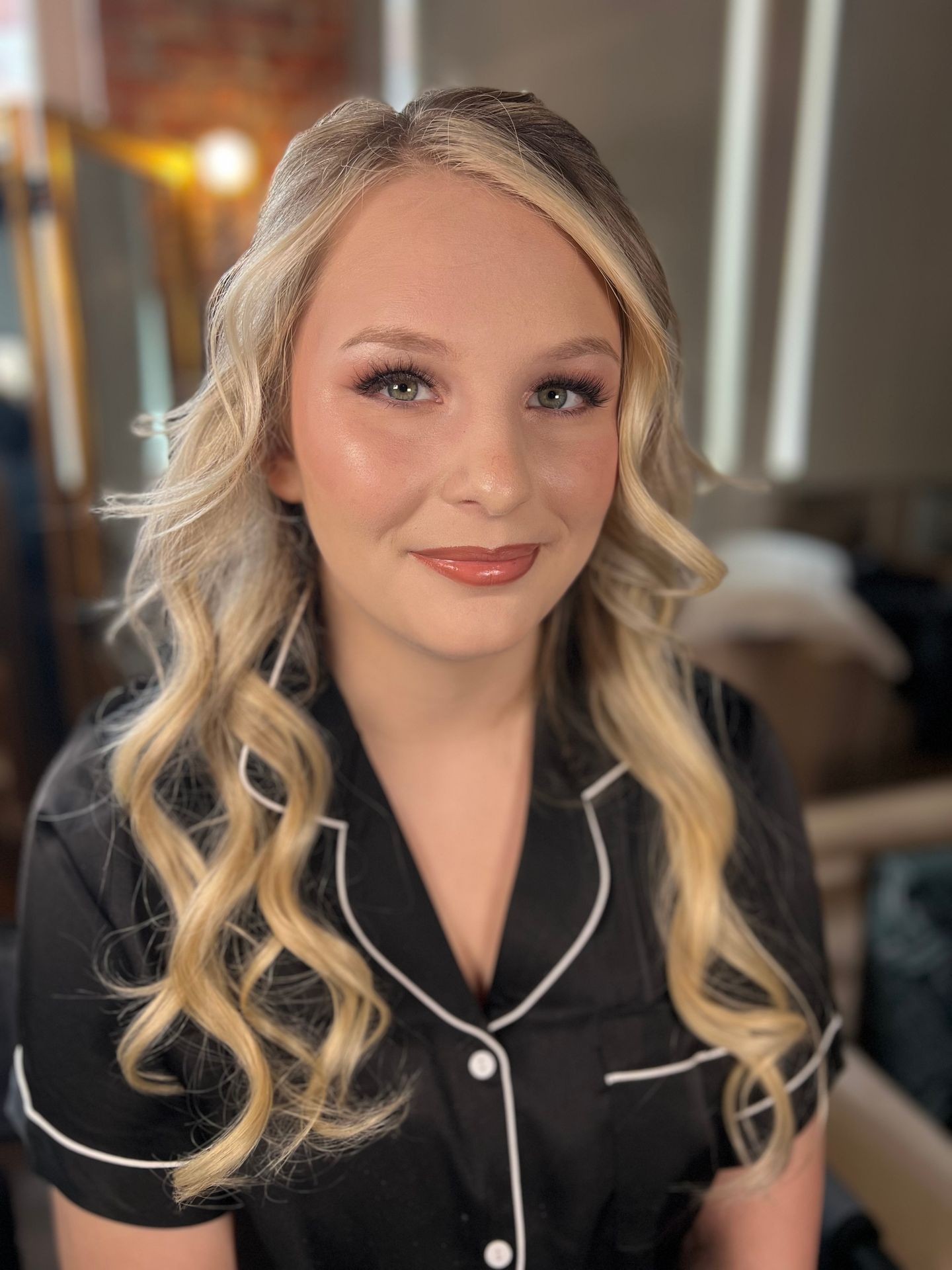 Smiling person with long wavy hair in a black shirt, seated indoors with soft lighting.